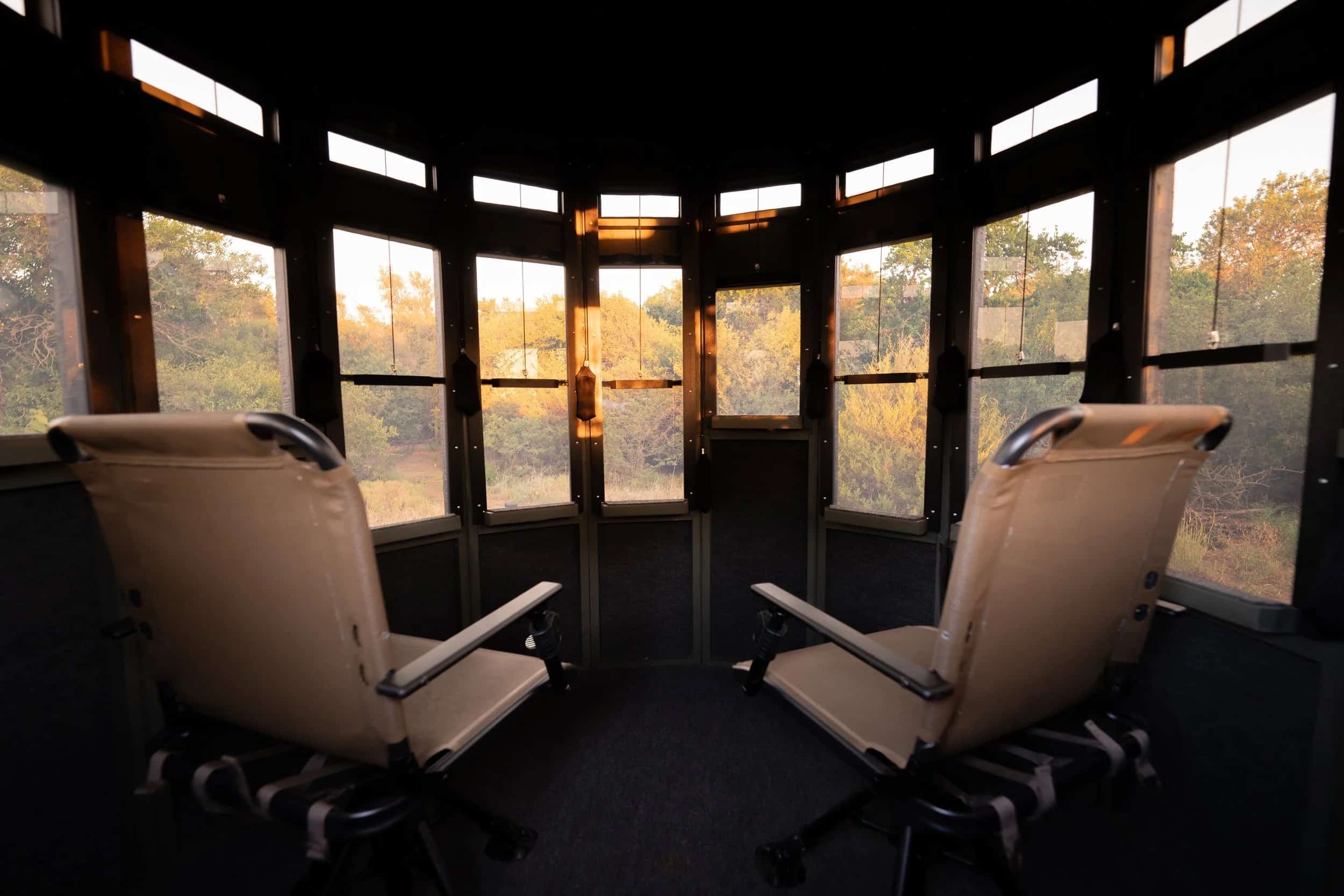 Interior view of the 360 Pro hunting blind with two chairs, showcasing large windows and a sunset outside.