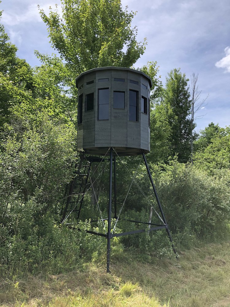 Green 360 Pro hunting blind on metal legs surrounded by trees and shrubs