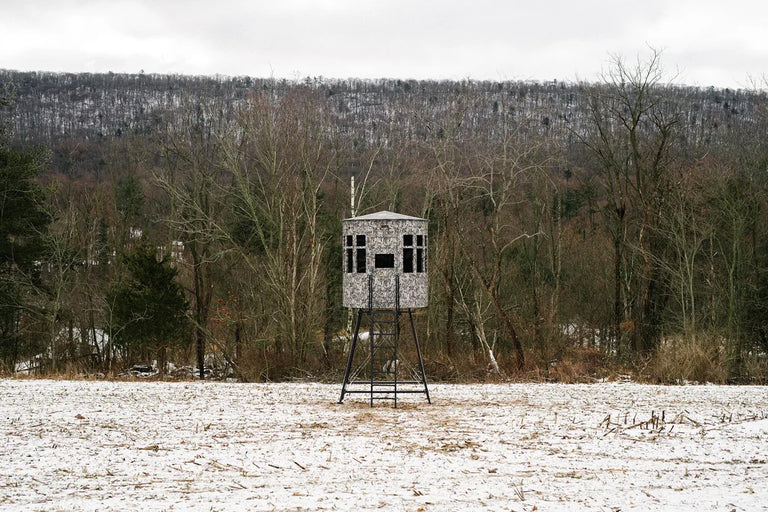 Wooden hunting blind on stilts in a snowy field with trees in the background, winter scene