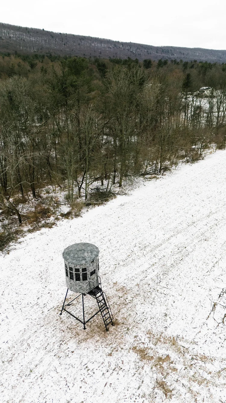 Snow-covered landscape with a hunting blind in a forested area, aerial view.